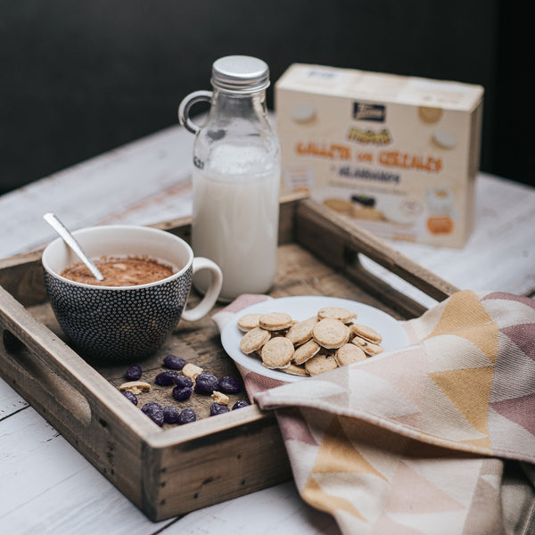 Tirma Cereal and Blueberry Mini Biscuit Semicovered with White Chocolate 160 g filled in a white plate next to the bottle of milk and a cup with spoon. Spanish biscuits made in Spain.