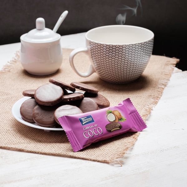 Coconut Biscuit covered in Milk Chocolate 200 g placed next to a cup and sugar with spoon, a plate filled with coconut milk chocolate biscuit. Spanish coconut biscuits made in Spain.
