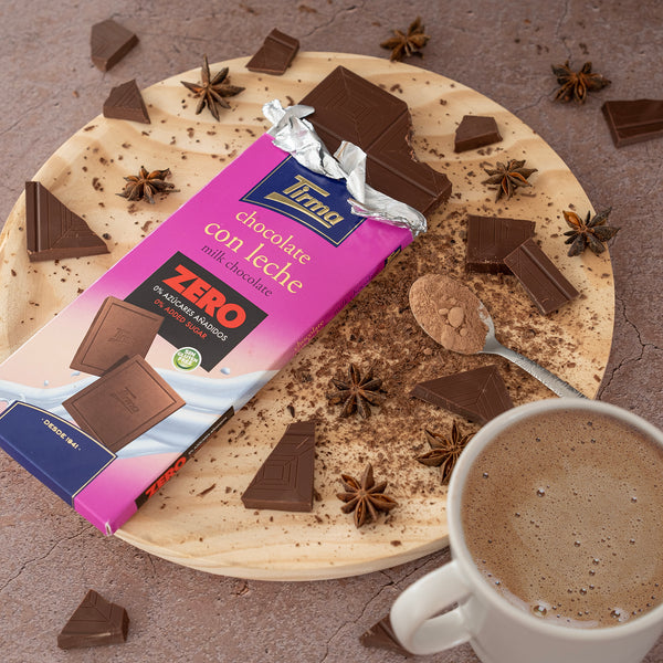 Tirma Zero Milk Chocolate Bar with No Added Sugars, 125g. Gluten Free chocolate on a wooden plate and a pieces of chocolate next to a cup of coffee and a spoon. Spanish chocolate made in Spain.