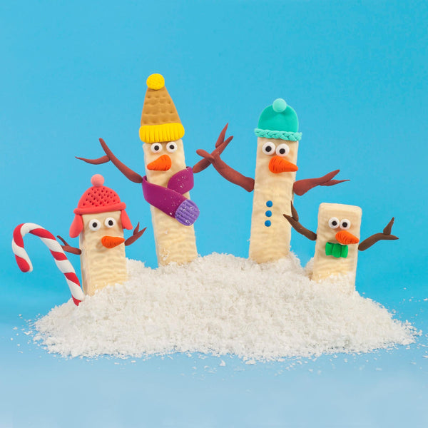 Four white chocolate wafers by Tirma, cream-filled, dressed up as colourful snow men and placed on desiccated coconut.