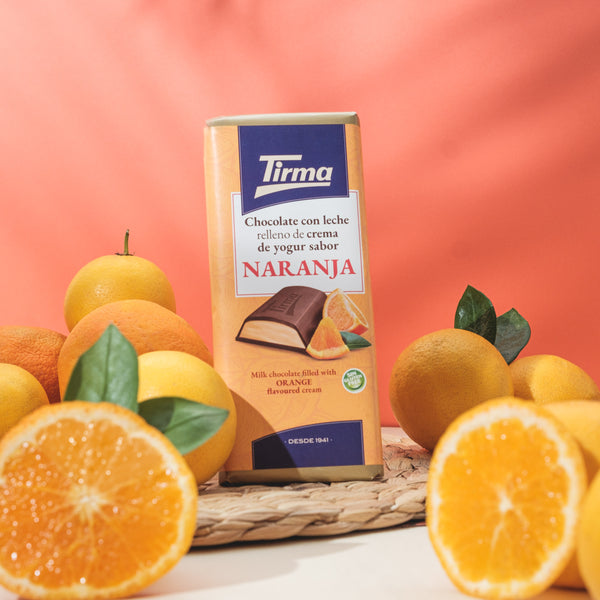 Tirma orange-flavored chocolate bar surrounded by oranges on a pink background