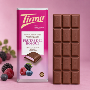 A bar of Tirma chocolate with fruit filling stands next to its pink packaging box on a pink background, with berries and grapes used as styling props.