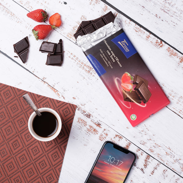 Tirma 70% Dark Chocolate with Strawberry Granules placed next to a cellphone and a cup of coffee with spoon. Spanish strawberry chocolate made in Spain.
