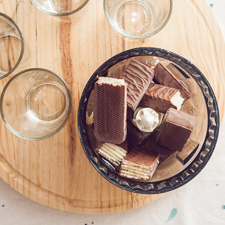 Multiple milk chocolate wafers broken in half and added to a grinder to add as topping on desserts. Placed on a wooden board with 4 cups.