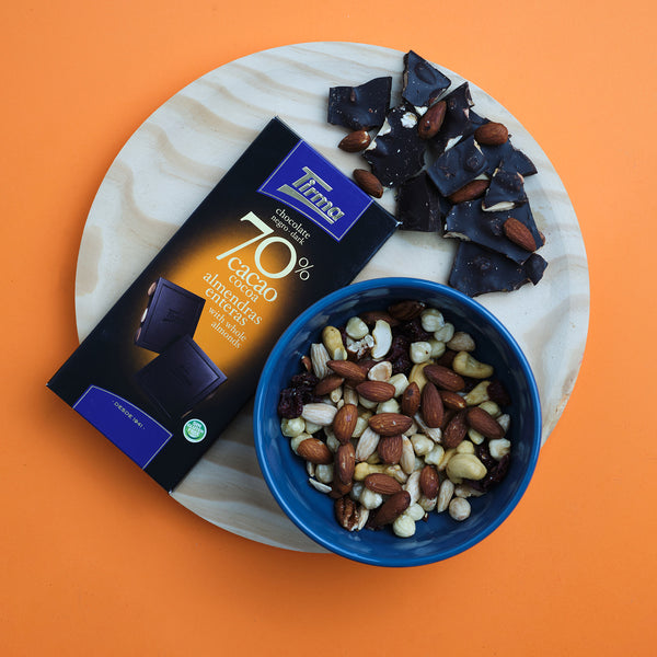Tirma 70% dark chocolate bar with whole almonds, 125g. Gluten Free Chocolate. Vegetarian Chocolate in orange background placed next with a bowl of almonds and cuts of chocolate bars. Delivery in the UK