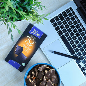 Tirma 70% dark chocolate bar with whole almonds, 125g. Gluten Free Chocolate placed next to the laptop and a ballpen. Spanish chocolate with almonds made in Spain.