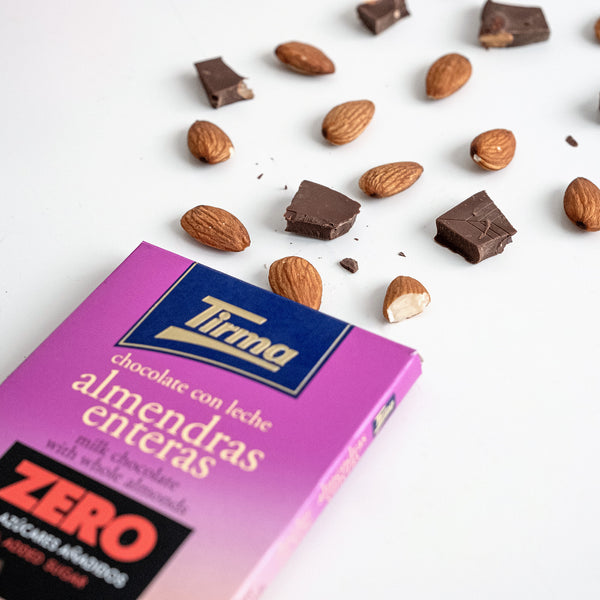 Close up of Tirma Milk Chocolate Bar with Whole Almonds, No Added Sugars, 125g. Surrounded by whole almonds and broken into pieces. Spanish chocolate made in Spain.
