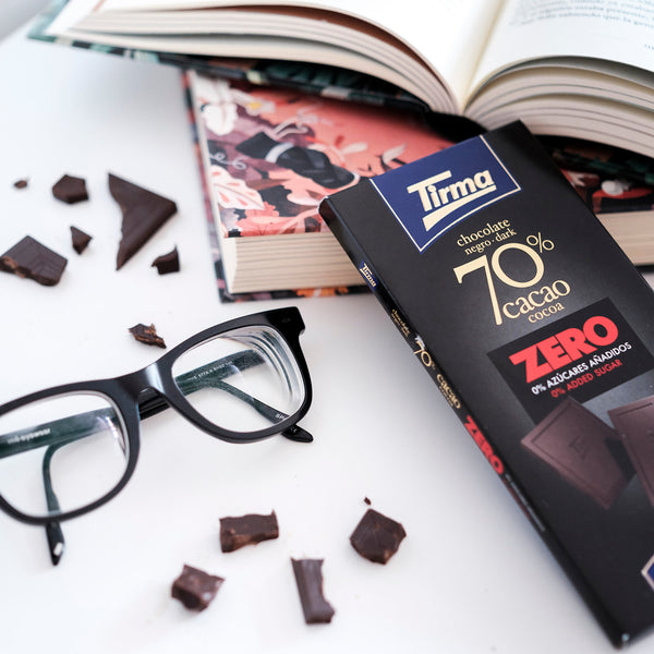 Tirma ZERO Dark Chocolate Bar 70% cocoa no added sugars and gluten free cuts placed next to the book and the reading glass. Spanish chocolate bar made in Spain.
