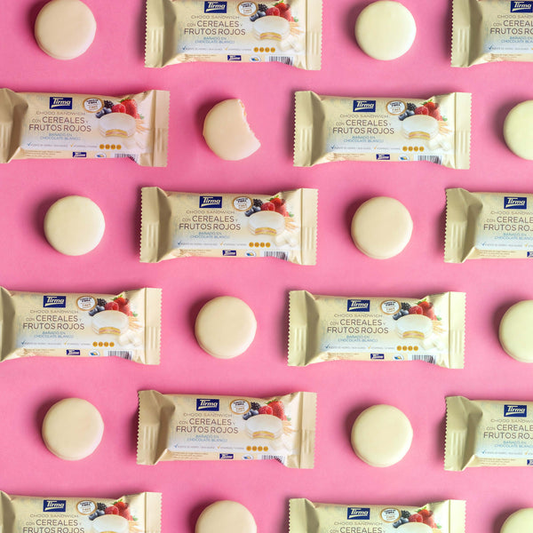 12 Tirma Cereal and Berry Chocolate Biscuit Sandwich Covered in White Chocolate placed next to organized round biscuits in a pink background. Spanish cereal biscuits made in Spain.