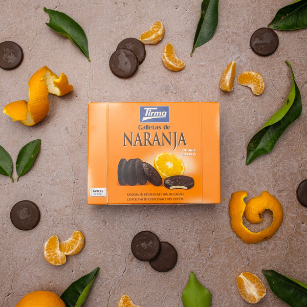 Tirma Orange Biscuits covered in 70% Dark Chocolate 200 g placed on the center next to leaves, peel of oranges and a chocolate orange biscuits. Spanish orange chocolate biscuit made in Spain.