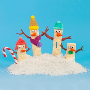 Four white chocolate wafers by Tirma, cream-filled, dressed up as colourful snow men and placed on desiccated coconut.